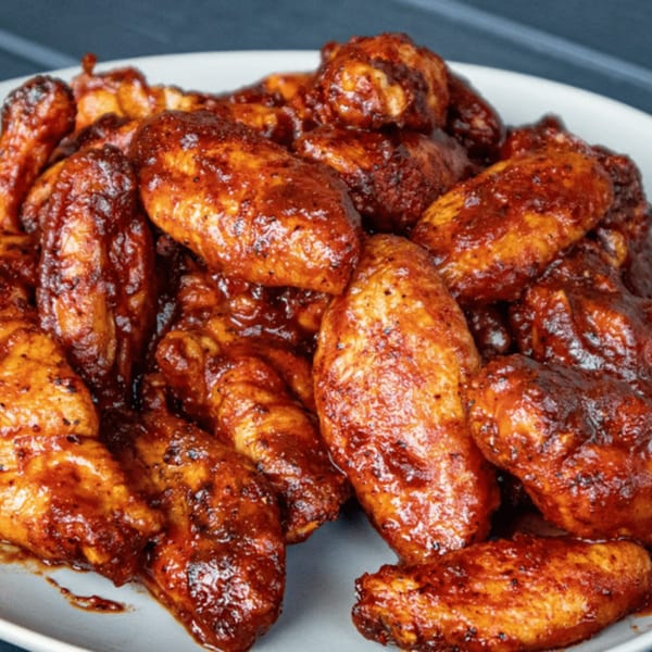 A white plate piled high with glistening, saucy BBQ chicken wings from Larry J's BBQ Cafe.