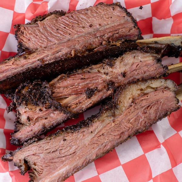 Larry J's BBQ Cafe's smoked beef ribs with a dark bark and pink smoke ring on red checkered paper.