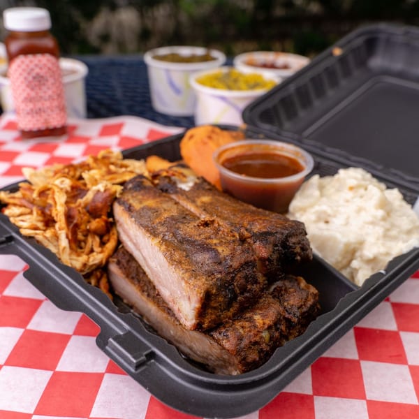 Larry J's BBQ ribs, pulled pork, potato salad, and sweet potato in a takeout container.