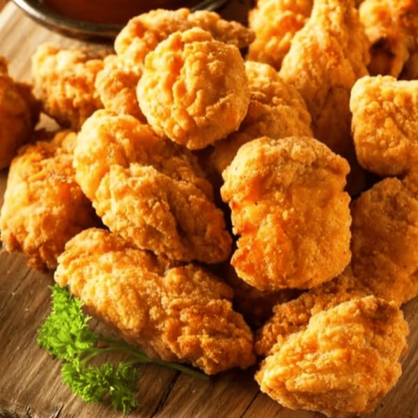 Golden-brown fried chicken nuggets, garnished with parsley, on a rustic wooden surface.