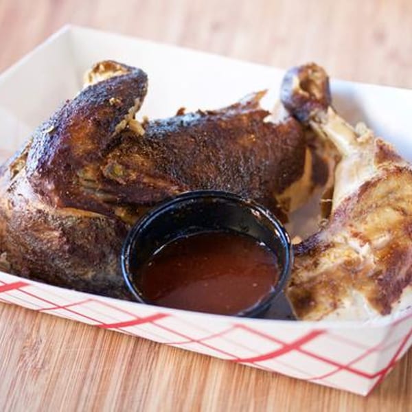 Larry J's BBQ Cafe's smoked chicken quarters with a side of barbecue sauce in a paper tray.